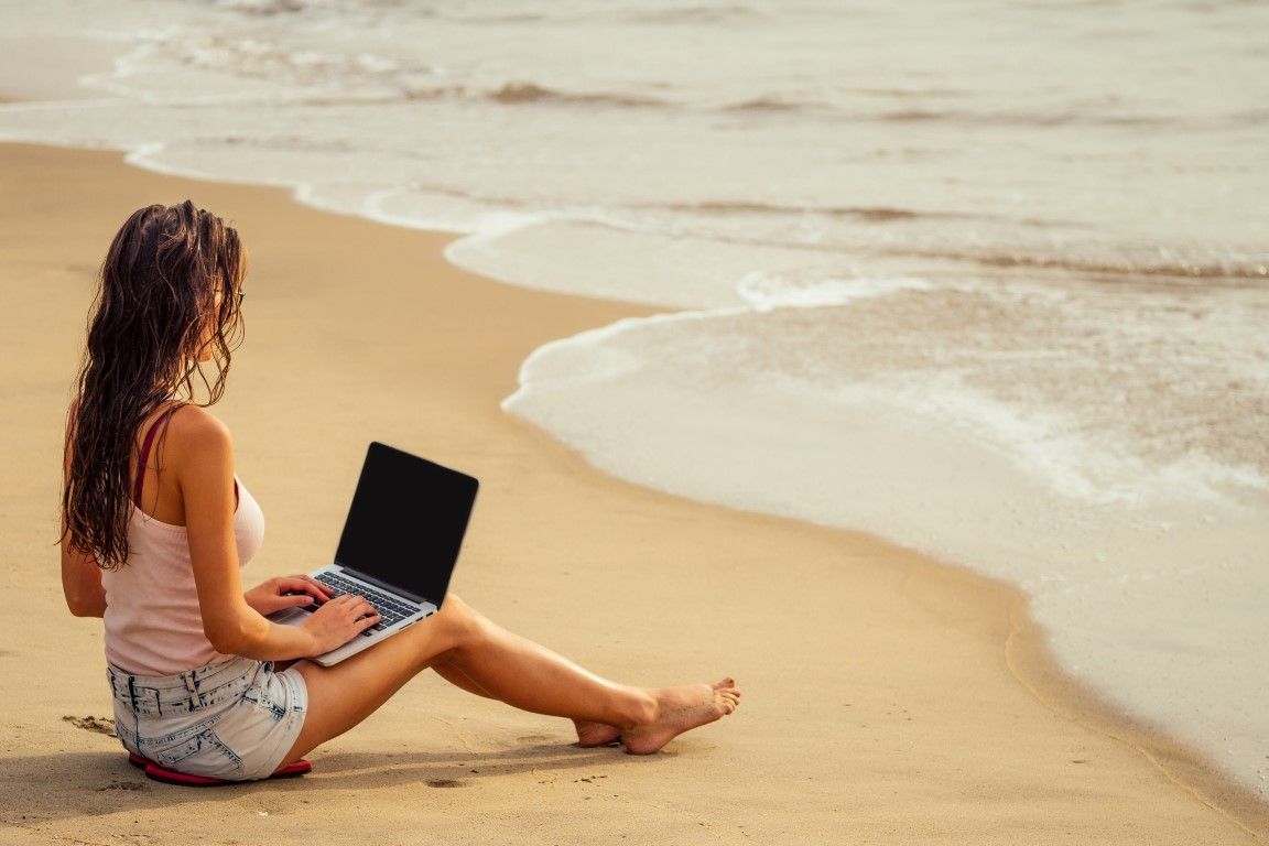 Young sexy woman in stylish glasses using laptop freelancing on the tropical paradise beach. Girl freelancer work sitting in a summer sand on the seashore remote work indian ocean background copyspace